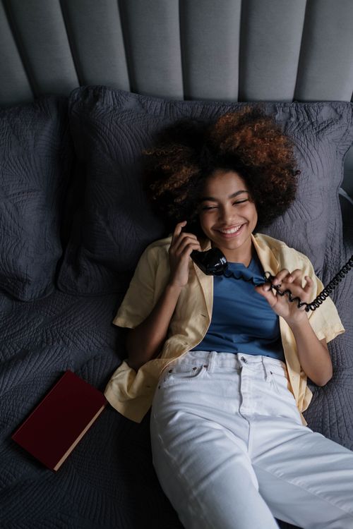 Free Smiling woman with afro hair chatting on phone, lounging comfortably on a bed. Stock Photo