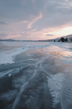 A serene view of a frosty, frozen lake surrounded by snow during sunset, capturing winter's beauty.