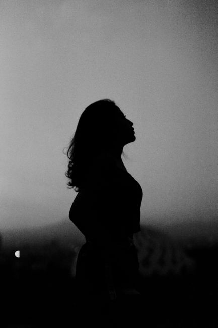 Artistic silhouette of a woman against a moody dusk sky, captured in monochrome tones.