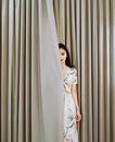 Woman in White and Red Floral Dress Standing Beside White Window Curtain