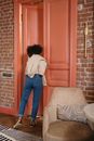 Woman in White Long Sleeve Shirt and Blue Denim Jeans Standing in Front of Brown Wooden