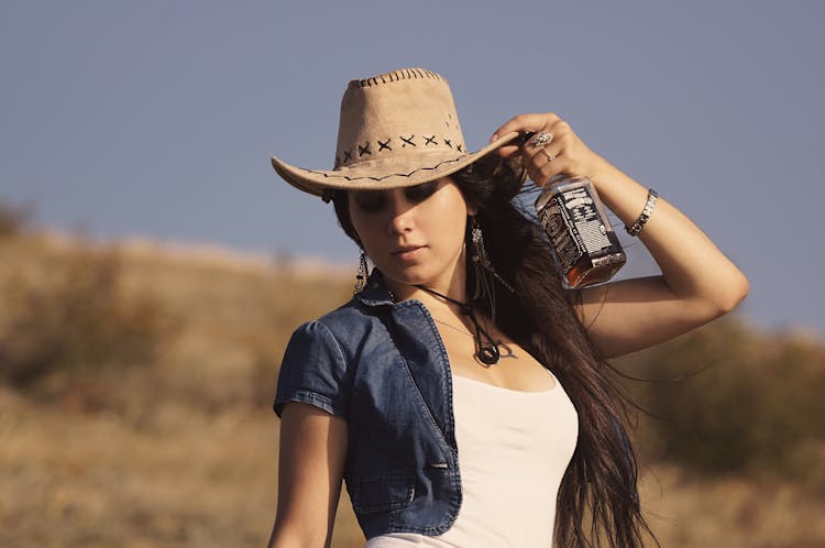 Woman Touching Her Hat While Holding A Bottle Of Whiskey