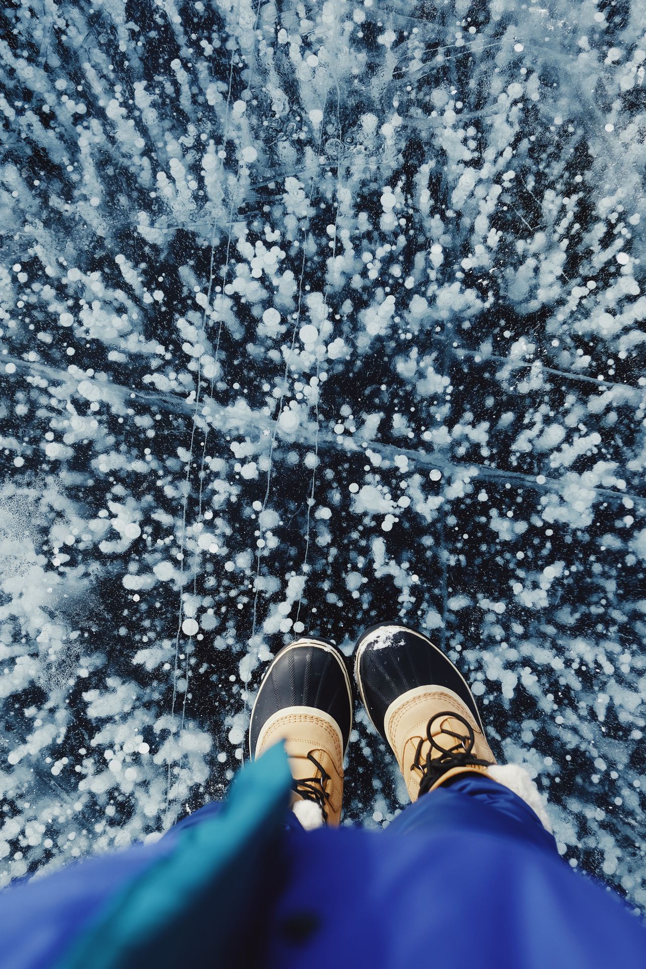 duck-style boots standing on a frozen lake with ice patterns