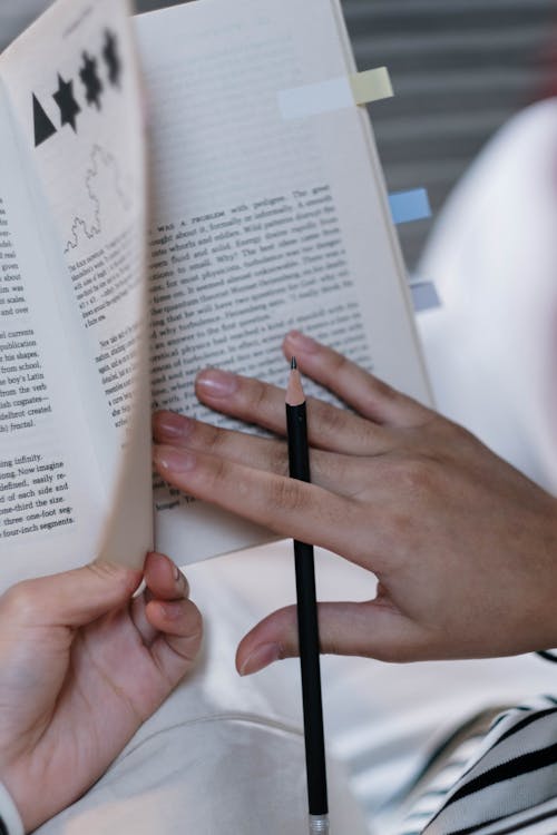 Close-up of Person Holding a Textbook and a Pencil 