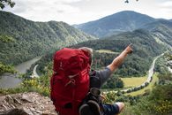 Person in Black Jacket and Red Backpack Standing on Rock