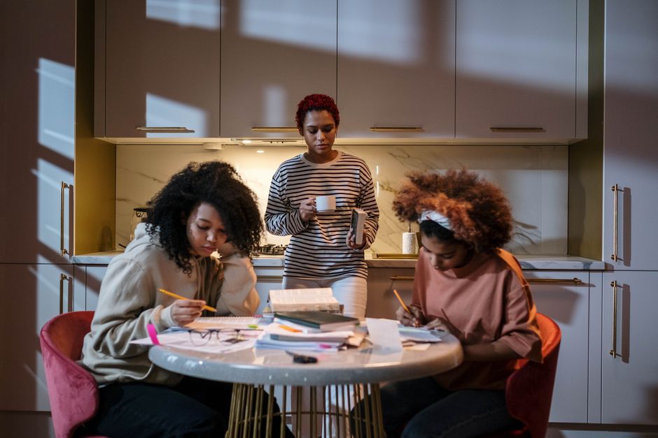 Three young women studying and enjoying coffee in a cozy kitchen, focused and engaged.