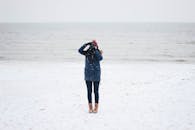 一个人在白雪覆盖的海滩上拍照，身后是海洋