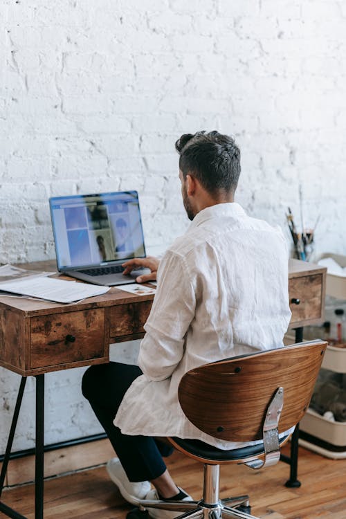 Back view unrecognizable male in formal wear working on modern netbook while sitting at desk in light room