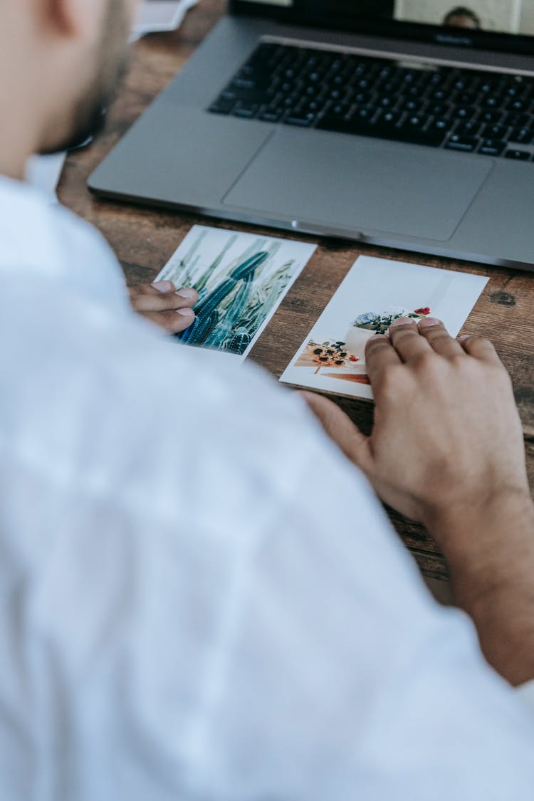 Crop Unrecognizable Man Looking At Printed Photos At Desk