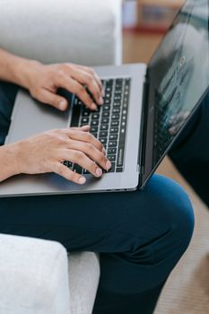 Crop anonymous male typing on netbook keyboard on laps while sitting on comfy armchair