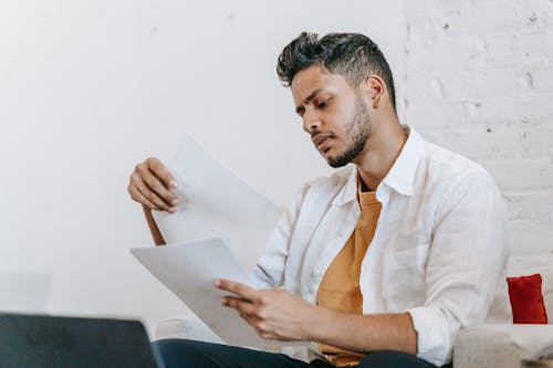 Attentive ethnic man reading documents on armchair