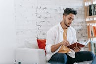 Attentive ethnic man reading notes in diary on armchair