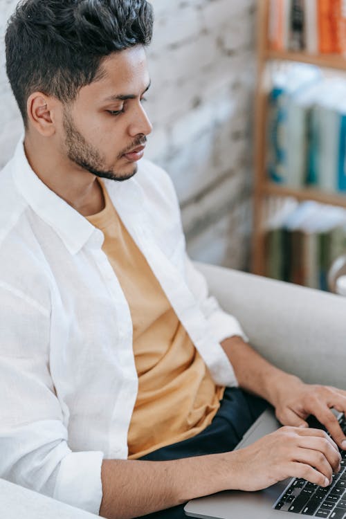 Crop focused ethnic man working on laptop on armchair