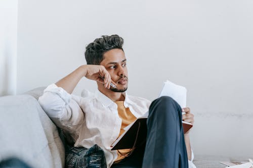 Unemotional ethnic man sitting on sofa with diary