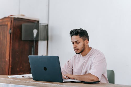 Serious Hispanic freelancer working on laptop at table in house