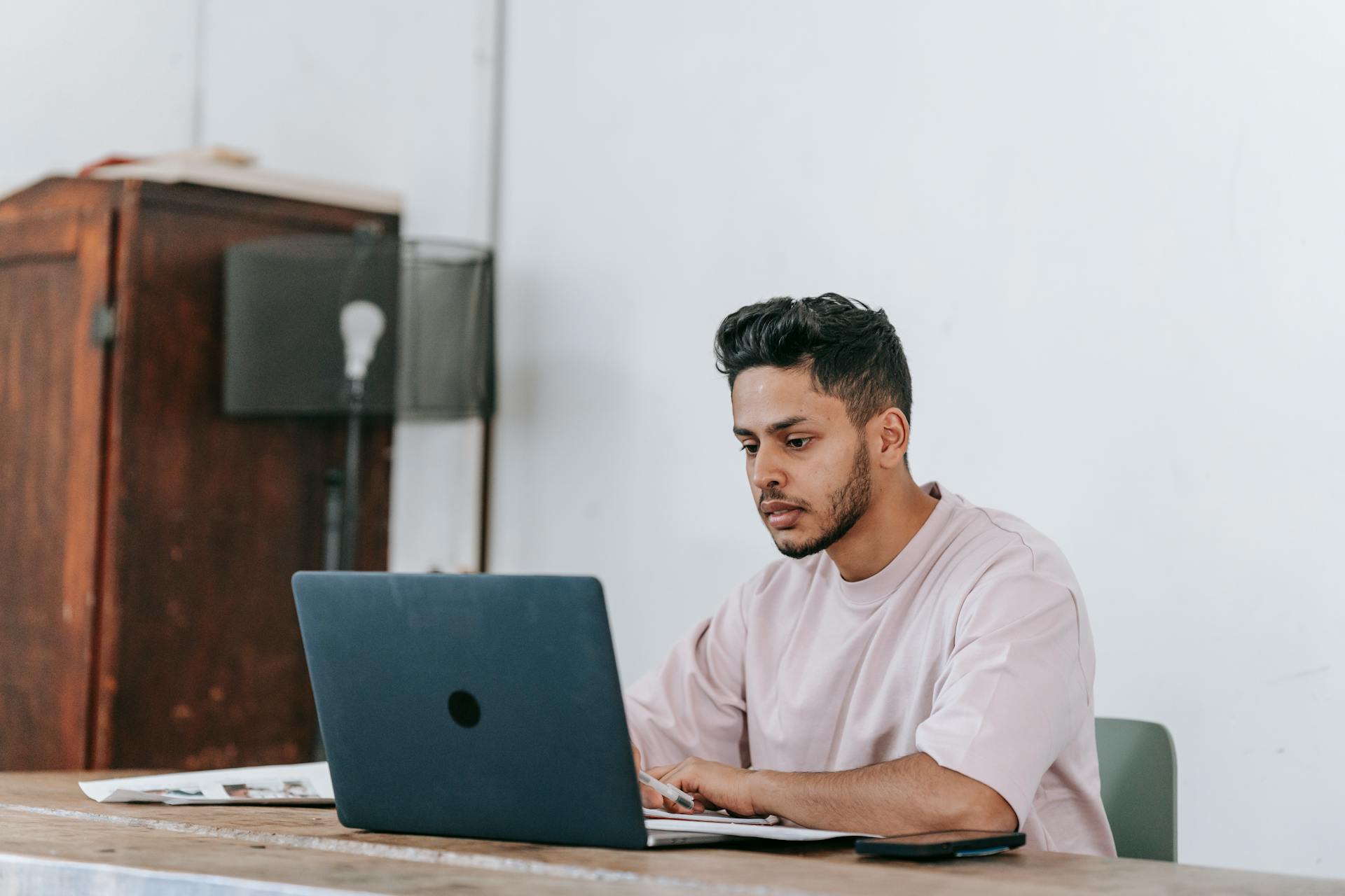 Serious Hispanic freelancer working on laptop at table in house