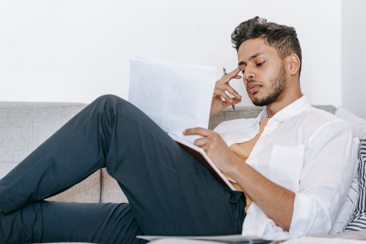 Thoughtful Hispanic Employee With Papers Working On Couch