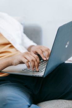 Crop anonymous male in casual clothes typing on netbook keyboard on laps and sitting on comfy couch