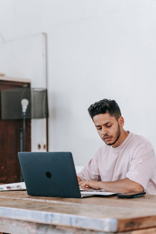 Free Concentrated young ethnic male in casual clothes browsing netbook and sitting at desk in light room Stock Photo