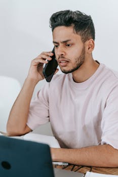 Young man with phone and laptop concentrating on freelance work.
