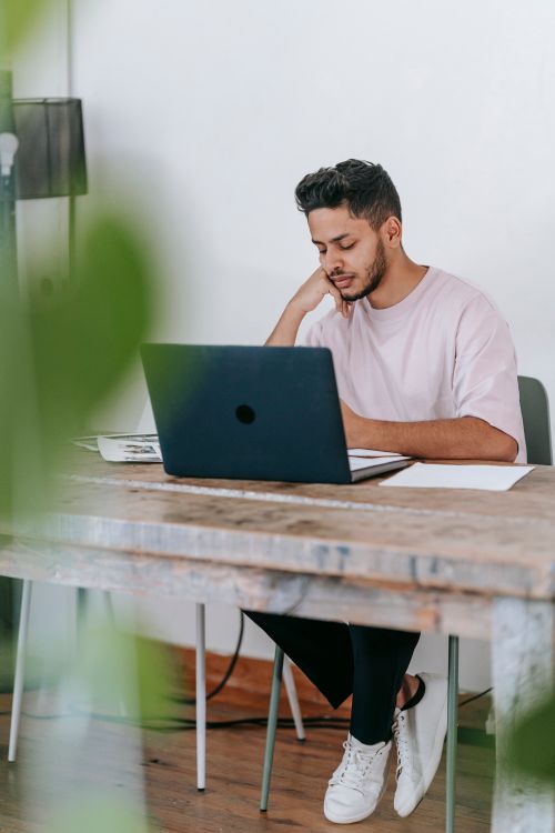 Free Full length concentrated ethnic male in casual clothes browsing modern netbook and sitting at desk Stock Photo