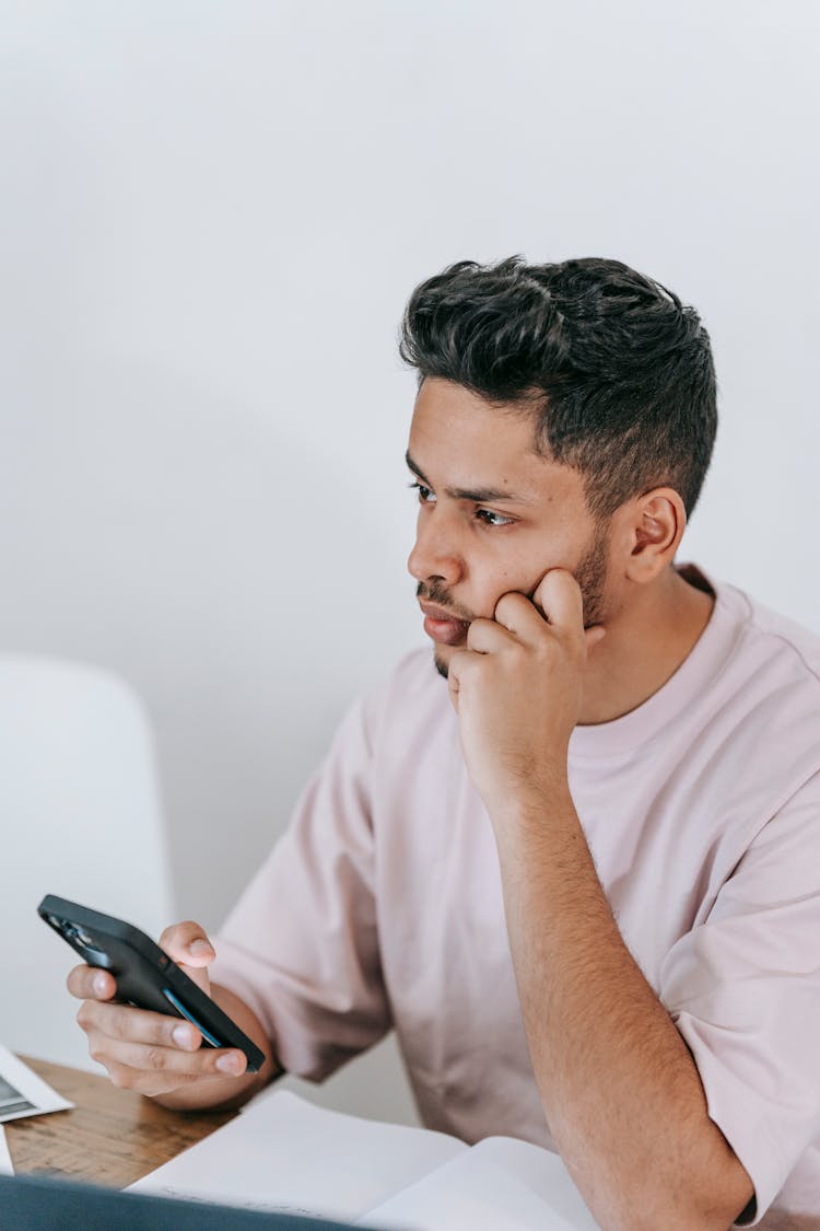 Pensive Ethnic Man Using Smartphone At Desk