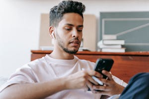 Ethnic man surfing smartphone and sitting in light room