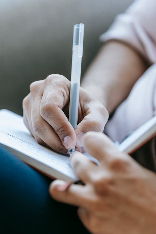 Free Crop anonymous person taking notes in diary placed on laps in light room Stock Photo