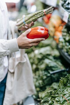 A customer selecting red bell pepper and asparagus at a grocery store.
