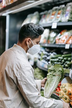 A man wearing a mask selecting fresh vegetables in a supermarket during the pandemic.
