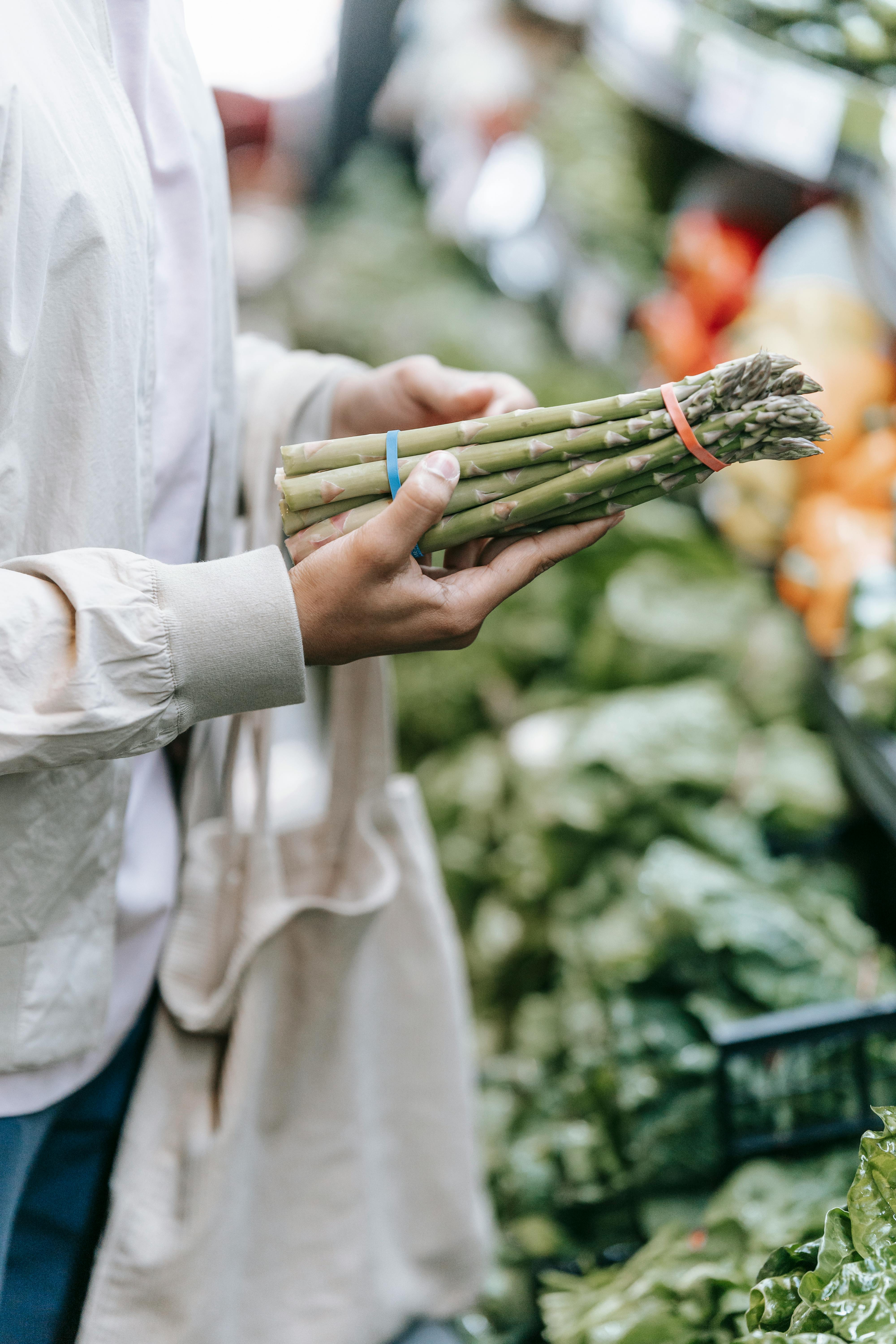 unrecognizable buyer picking asparagus in supermarket