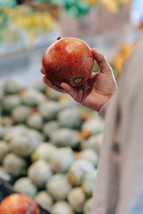 Crop male buyer choosing pomegranate in grocery market