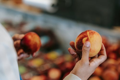 Crop faceless male choosing peaches in food market