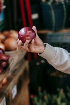 Crop anonymous man holding fresh red onion while choosing vegetables during shopping in grocery market