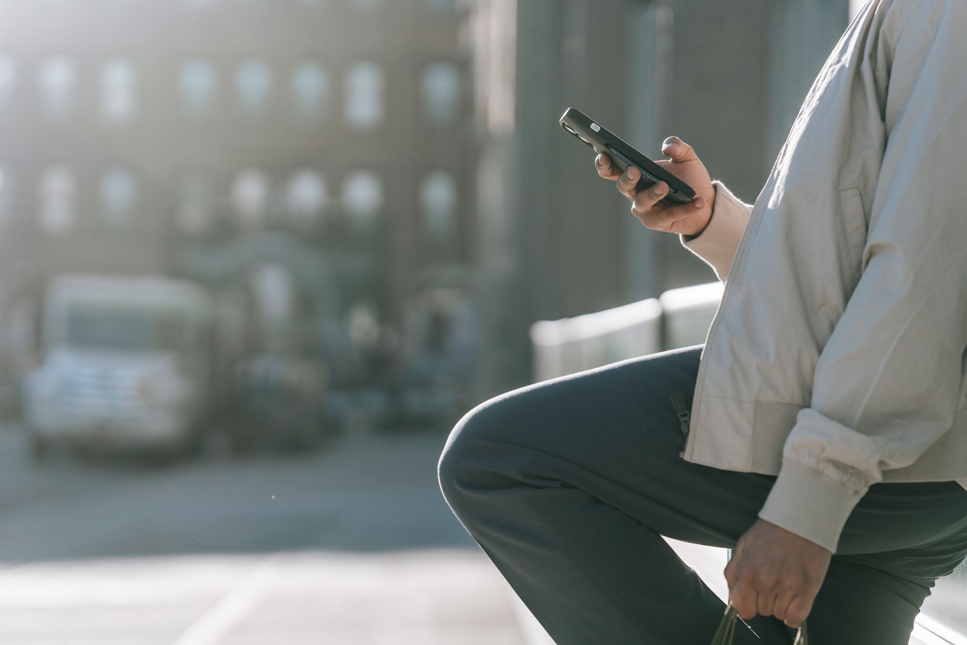 Side view of crop unrecognizable male with raised leg surfing internet on cellphone on roadway in sunny city