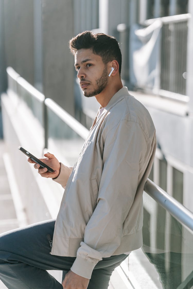 Indian Man In Earbud With Smartphone On City Street