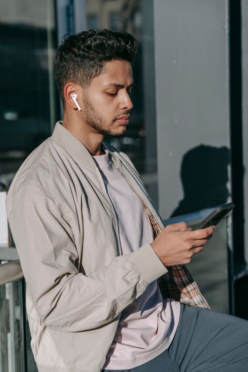 Man Calling Using Earbud Indian man with smartphone listening to music from earbud outdoors ...
