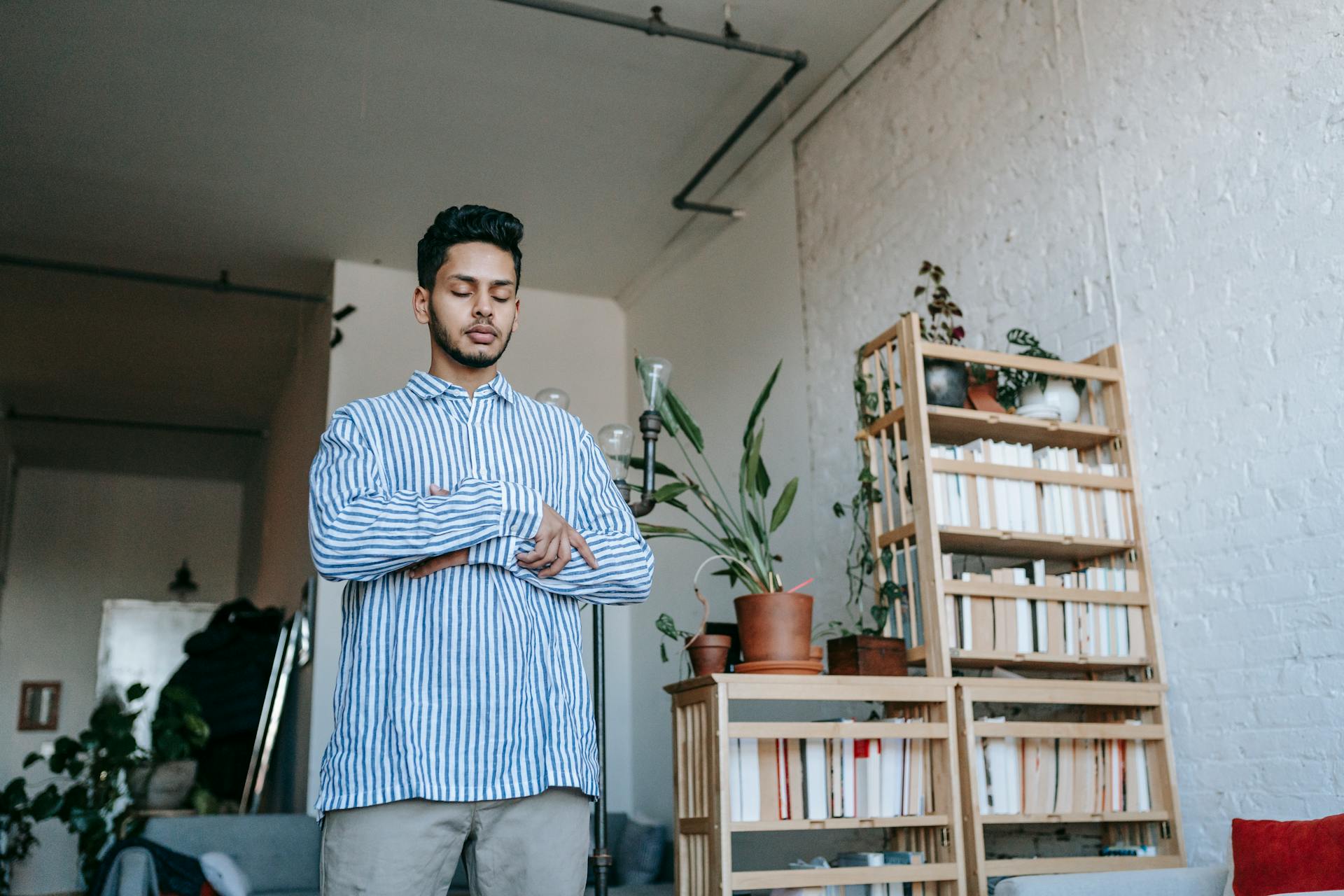 A young man practices mindfulness and meditation in a cozy indoor setting with plants and books.