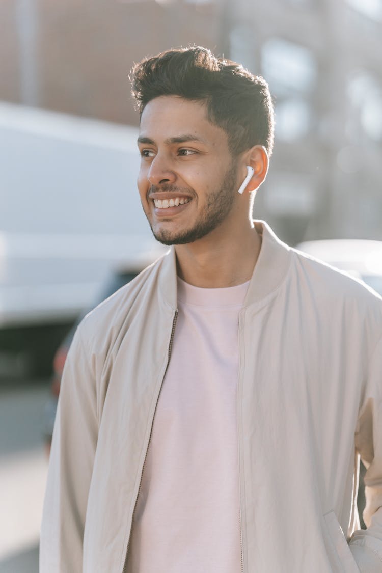 Smiling Ethnic Man Listening To Song From Earbud On Street