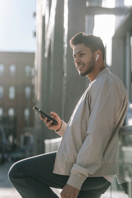 Man Calling Using Earbud Cheerful Indian man in earbud with smartphone on city street · Free ...