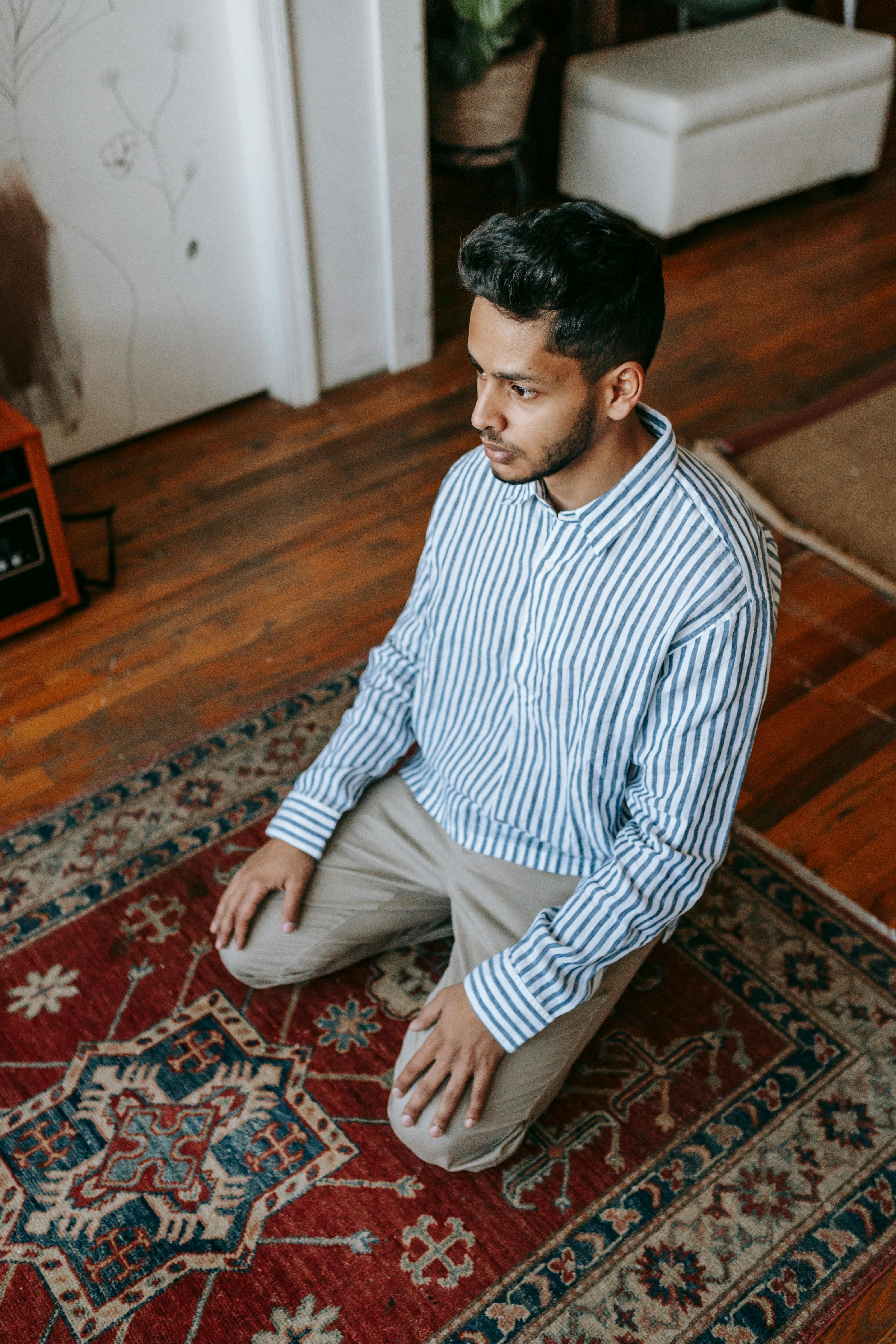 man in white and blue striped dress shirt kneeling on area rug