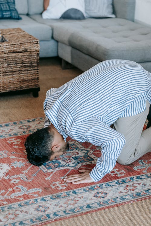 Man in Blue and White Stripe Dress Shirt Bowing Down on Red and Blue Area Rug