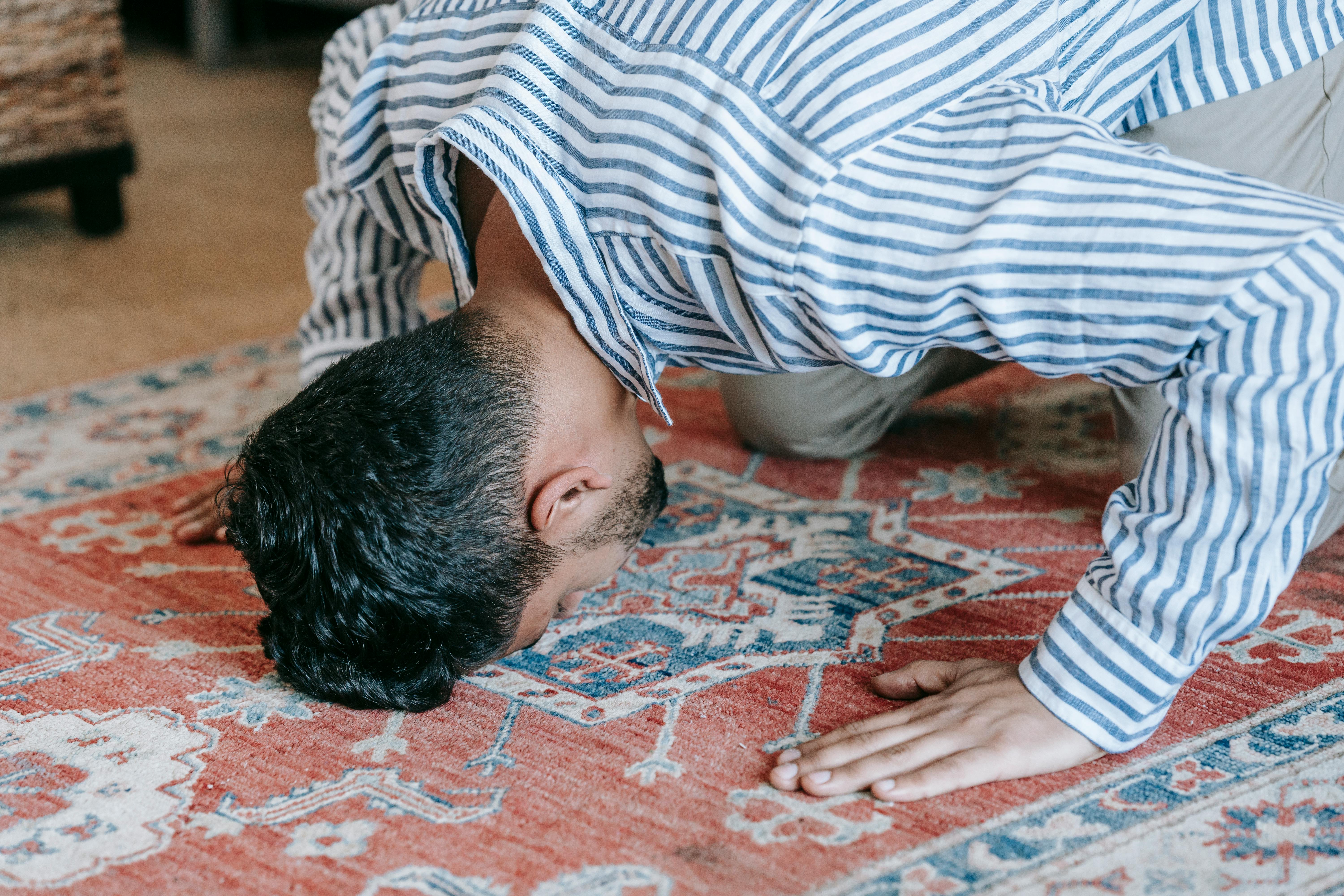 man in blue and white stripe dress shirt bowing down on red and blue area rug