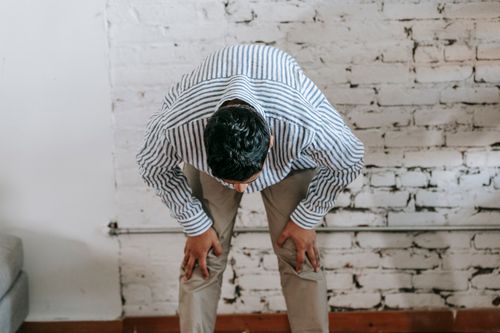 Free A man in casual attire bowing in a room with a white brick wall. Indoor setting. Stock Photo