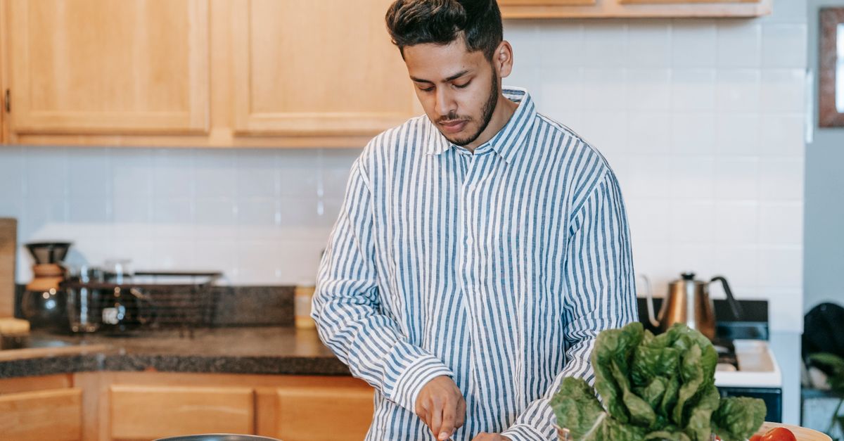 Jovem cortando legumes em uma cozinha moderna, enfatizando a culinária saudável.