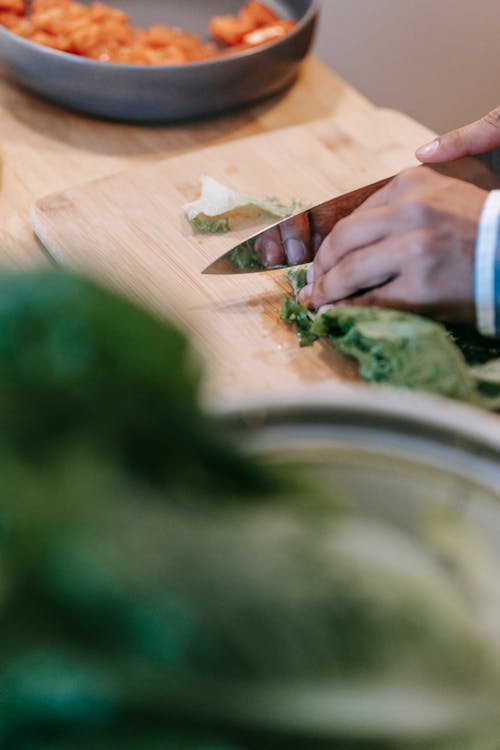 Crop person cutting fresh spinach on chopping board