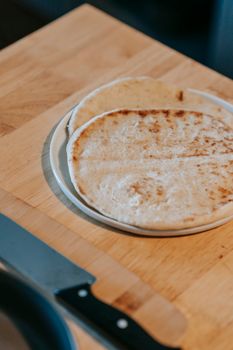 Tasty flatbreads on round plate against knife on chopping board on wooden table at home