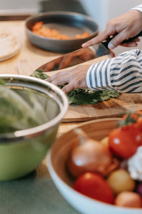 Crop man cutting fresh spinach on chopping board in kitchen