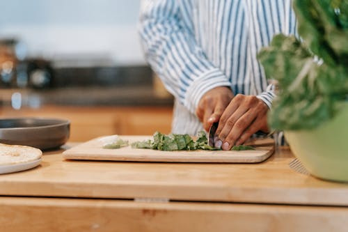 Faceless ethnic man cutting spinach leaves in house kitchen