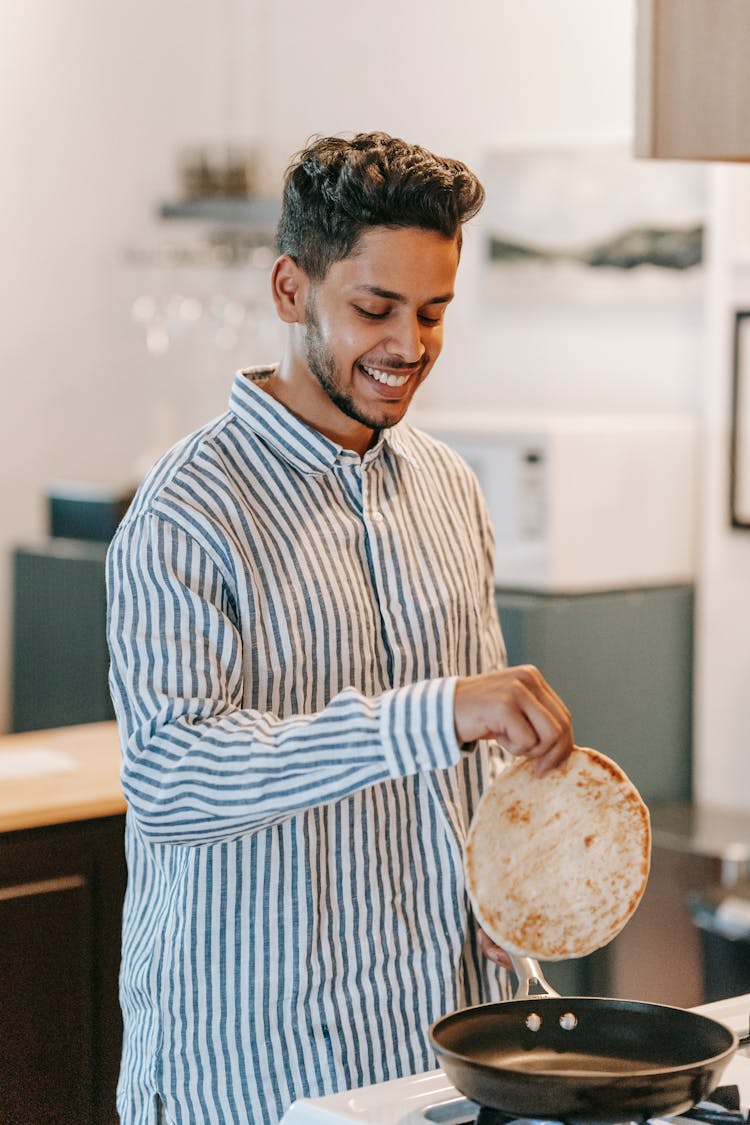 Smiling Indian Man With Flatbread Above Pan On Stove